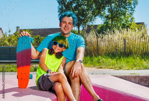 Blue hair father sit with a boy at skatepark, hold skateboard © Sergey Novikov