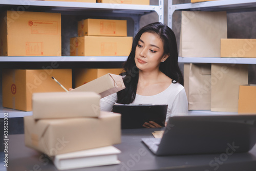 Asian Start-up businesswoman cheking serial number of boxes with checklist Freelancers picking up a product to recheck an order. Entrepreneur SME working with box at home. Concept working at home. © Irin