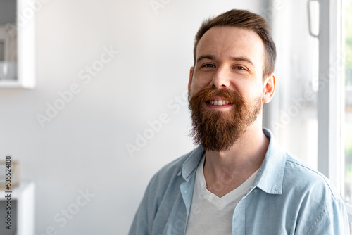 Bearded smiling handsome young man standing alone at home