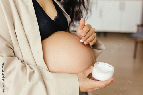 A pregnant girl in home clothes prepares healthy food.