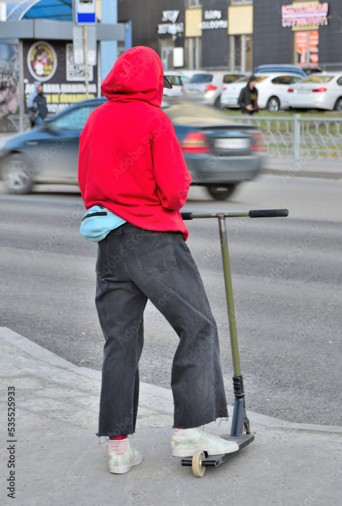 © vladimir subbotin - A woman with a scooter is waiting for a permissive light at the crossing on an autumn day