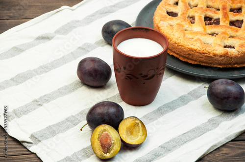 shortbread cookies with plums and a glass of milk on a wooden table. concept of homemade shortcrust pastry. baked fruit dessert on the kitchen table with a drink close up