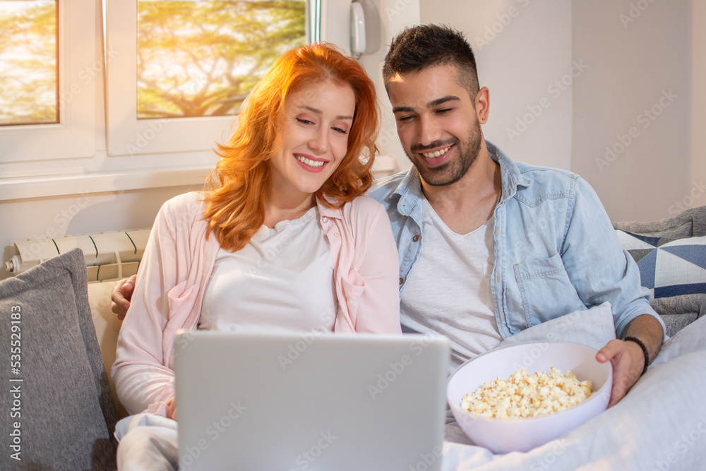 Cute young happy couple watching movie together and eating popcorn while sitting on sofa. Cute young happy couple watching movie together and eating popcorn while sitting on sofa.