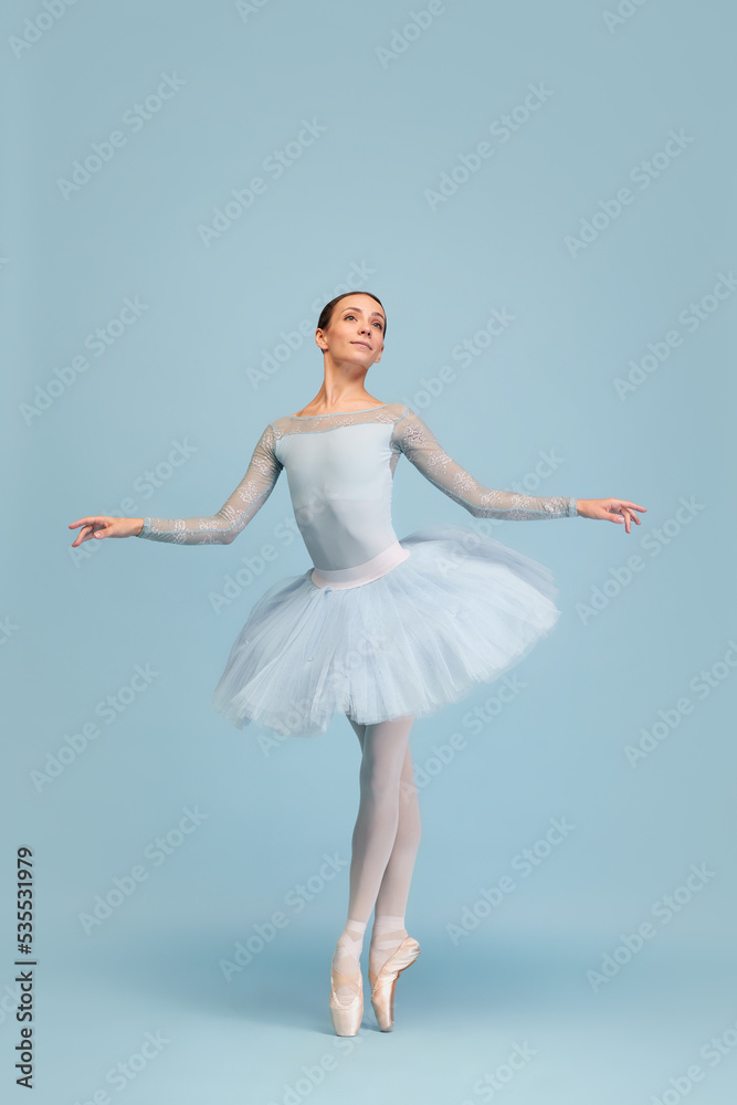 Naklejka premium Portrait of tender young ballerina dancing, performing isolated over blue studio background. Beauty of classical dance