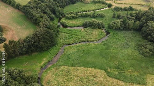Beautyful landscape from above showing a river floating through green fields filmed by a drone