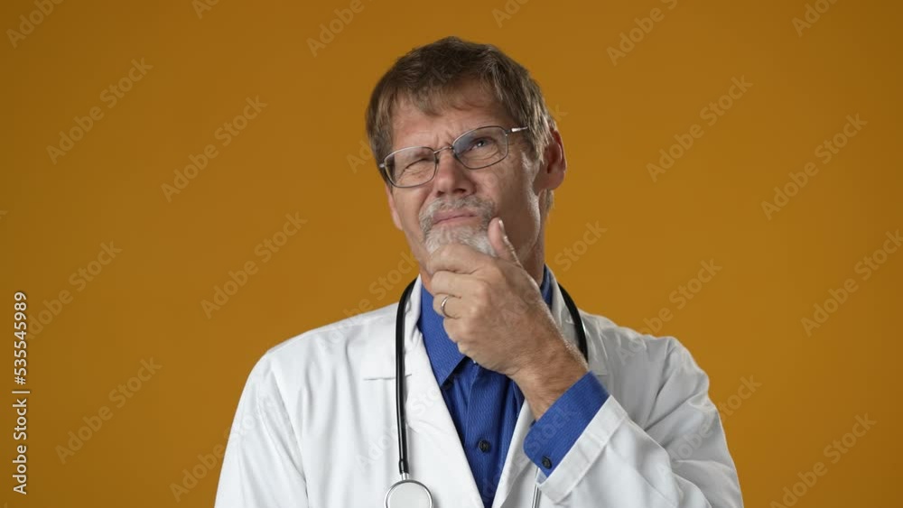Portrait of thinking pondering doctor man in medical coat having idea moment giving thumbs up on solid yellow studio background. Smiling happy doc showing eureka