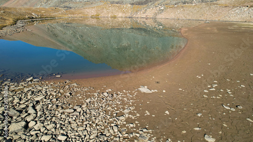 The emerald color of the water of a mountain lake. Drone view of a green mountain lake with a reflection of the mountains. Smooth transparent water. There are large stones nearby. Dry grass Kazakhstan photo