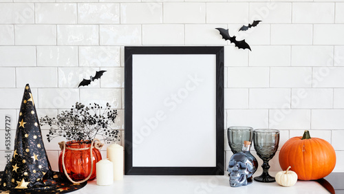 Black picture frame mockup with Halloween decorations on table on brick wall background. Scandinavian home interior design. Halloween holiday celebration concept. photo