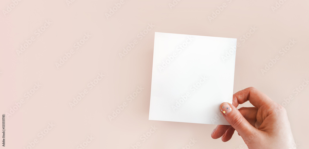 Obraz premium Banner of female hand with festive minimalistic natural manicure holding white piece of paper for notes with space for text. Concept of creativity, holiday wish, plans for future, art. Copy space