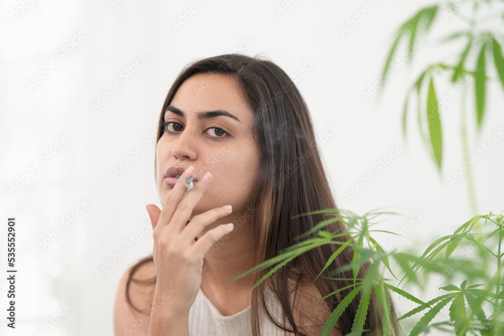 Asian woman smoking a marijuana weed joint, inhaling cannabis smoke. Asian woman smoking a marijuana weed joint, inhaling cannabis smoke.