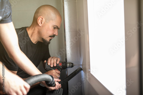 Man drills holes in the bathroom tiles to place the bathroom accessories