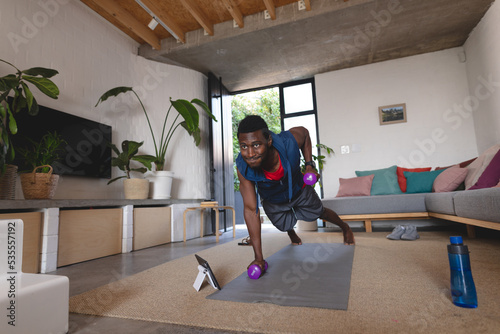 Happy african american man exercising, using tablet in living room