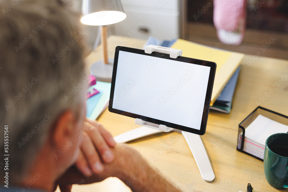 Caucasian man sitting at table in kitchen and using tablet with copyspace Caucasian man sitting at table in kitchen and using tablet with copyspace