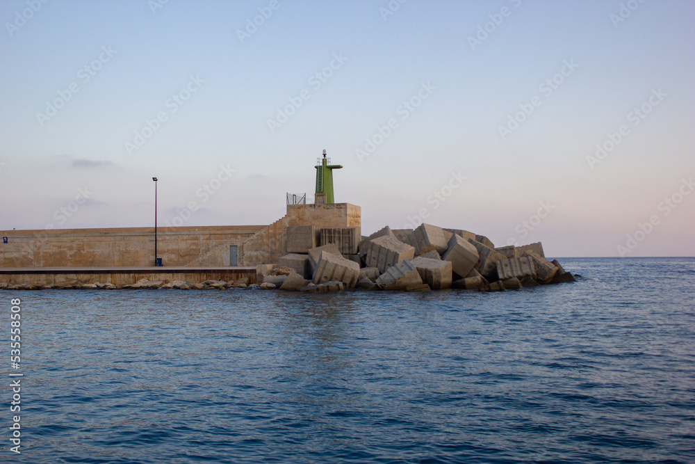Green lighthouse on wall with rocks seen from the sea
