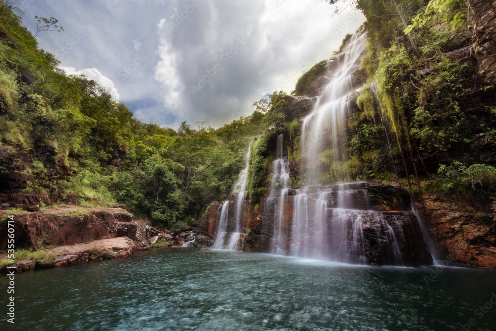 Fototapeta premium Beautiful waterfall in the middle of the forest softly lit by the sun on a cloudy day
