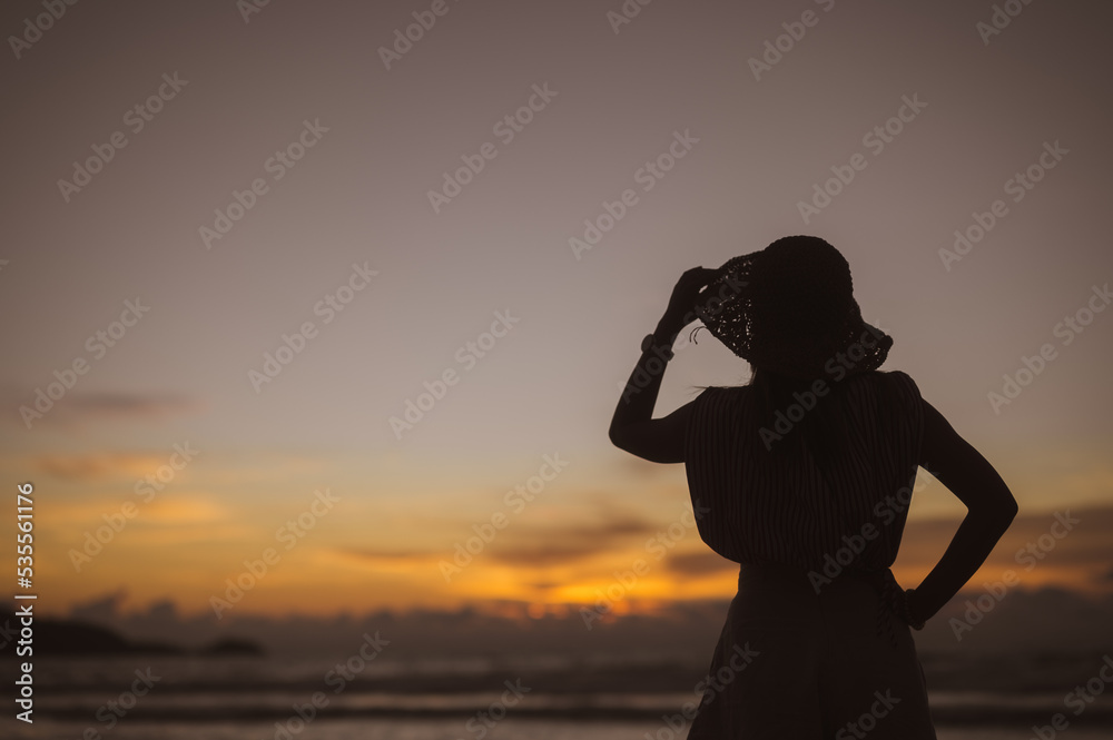 Silhouette of woman in hat on sunset background