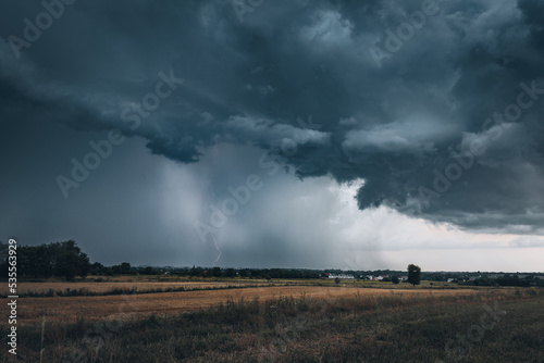 A huge storm cloud with a wall of rain in the countryside.