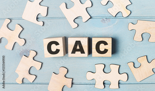 Blank puzzles and wooden cubes with the text CAC Customer Acquisition Cost lie on a light blue background.