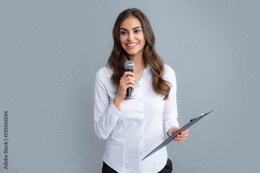 Portrait of young smiling business woman doing presentation with clipboard and microphone isolated grey background. Portrait of young smiling business woman doing presentation with clipboard and microphone isolated grey background.
