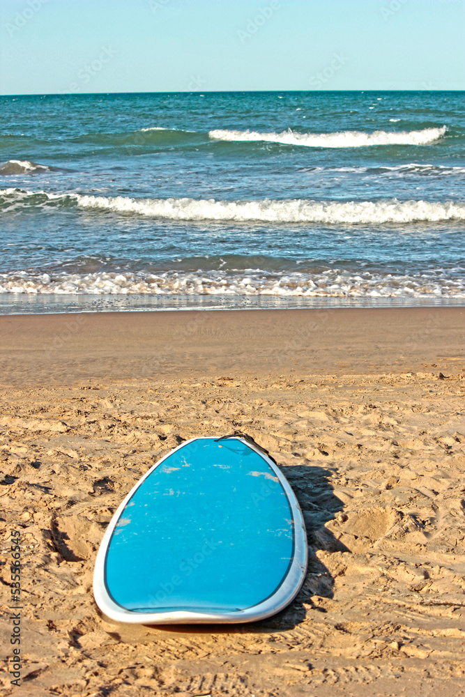 Surfboard on the sand of a beach with good waves and a clear sky Surfboard on the sand of a beach with good waves and a clear sky