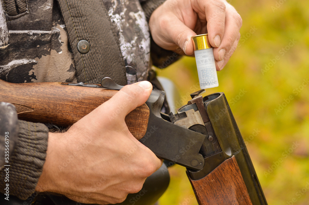 Selective focus of the hands of a man in a camouflage protective suit who loads a double-barreled shotgun. The concept of hunting. Selective focus of the hands of a man in a camouflage protective suit who loads a double-barreled shotgun. The concept of hunting.