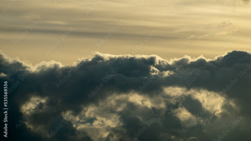 Obraz premium Fluffy yellow clouds after storm going over the horizon. Dark cloudy sky before thunderstorm panoramic background. Storm heaven panorama. Wide gloomy backdrop. Dramatic panorama sky