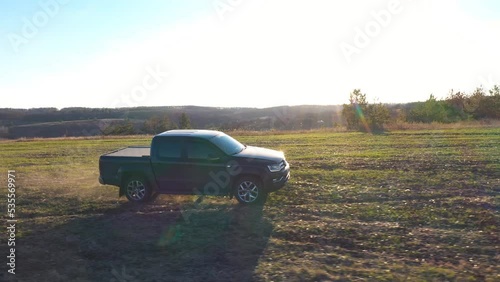 Aerial shot of pickup truck driving along meadow at summer day. Black car riding through field after harvesting. Flying over off road vehicle moving on farmland. Beautiful sunlight at background photo