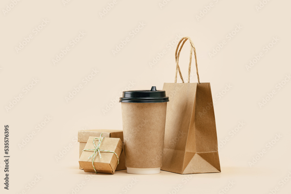 Takeaway paper coffee cup with lunch bag and bonus gift box on beige. Snack  delivery service.