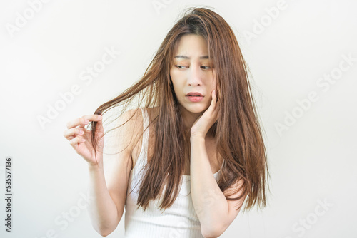 Damaged Hair, frustrated asian young woman, girl hand in holding splitting ends, messy unbrushed dry hair with face shock, long disheveled hair, health care of beauty. Portrait isolated on background.