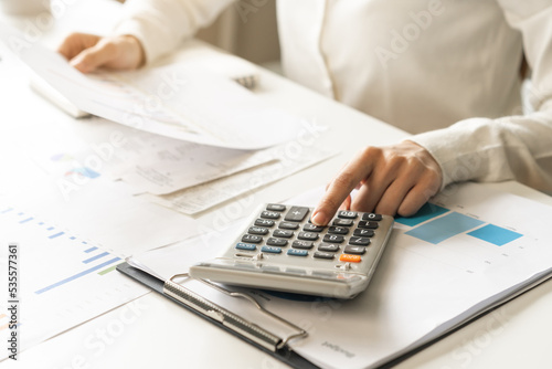 Account finance, asian young business woman hand use calculator for calculate budget, cost and income of company from bills, reports paperwork, plan spend money expenses, working on desk at home. © KMPZZZ