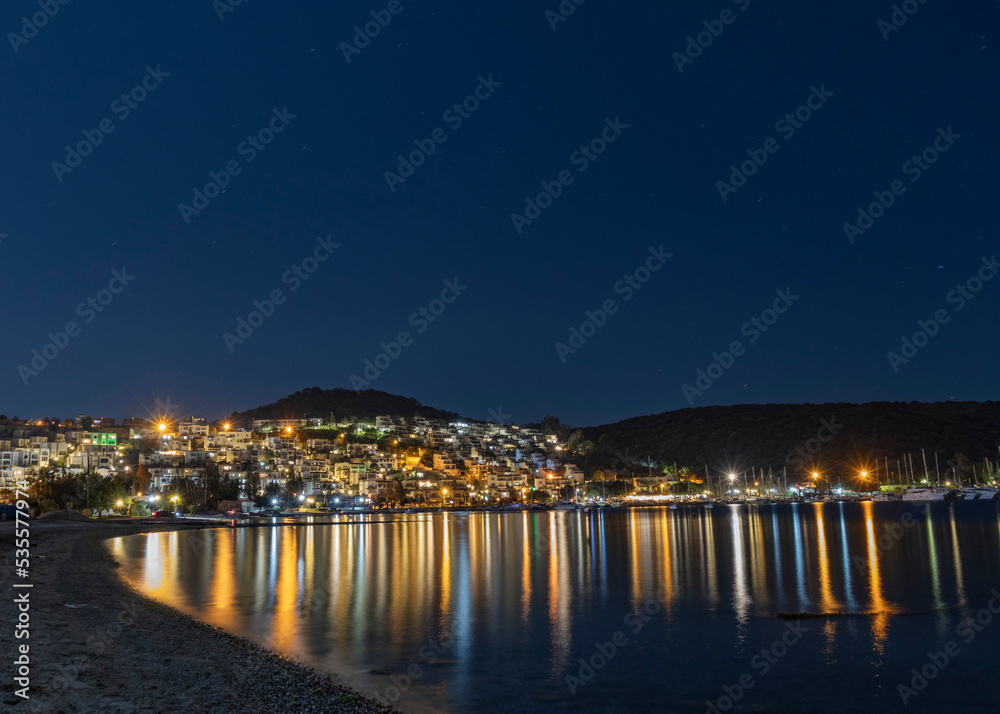 The empty beach at night, the calm sea and the reflection of the lights of the houses on the sea. Bodrum, Bitez.