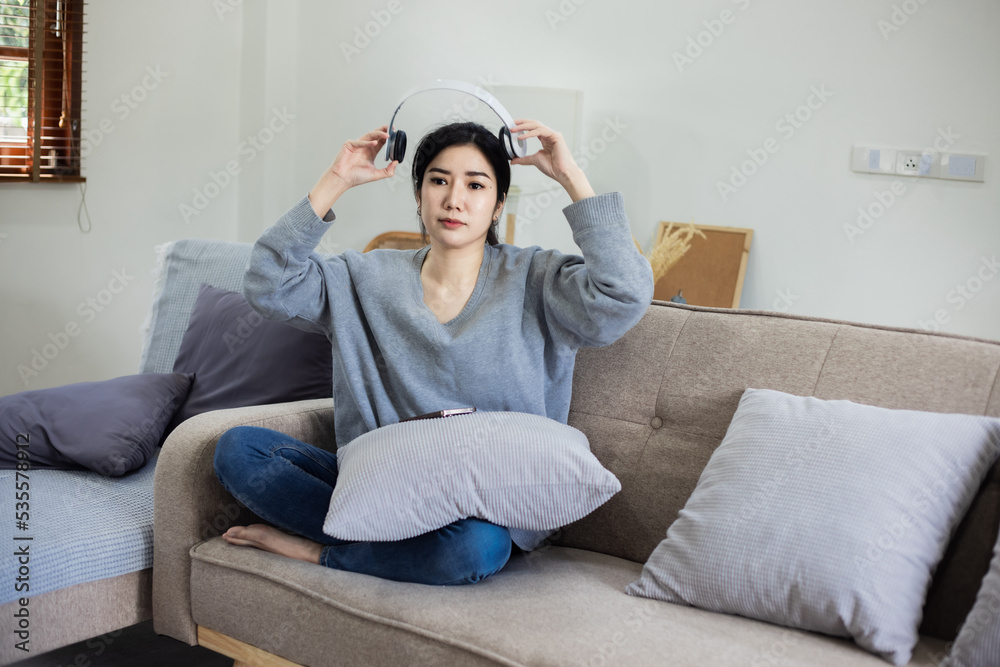 Happy Asian young woman wearing headphones sitting relaxing on sofa at home. Happy Asian young woman wearing headphones sitting relaxing on sofa at home.