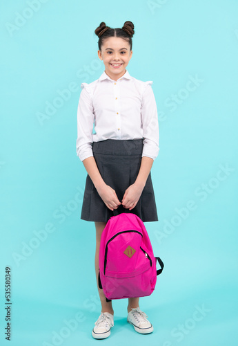 Back to school. Teenager schoolgirl in school uniform with backpack. School children on isolated blue studio background. Happy teenager, positive and smiling emotions of teen girl.