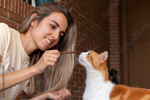 Young woman smiling while educating her cat pet with a treat in the front patio
