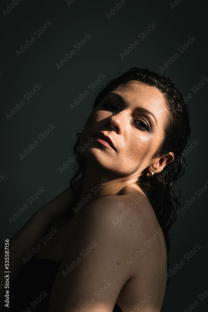 portrait of a beautiful brunette woman with a wet hairstyle in the sunlight in the dark. portrait of a beautiful brunette woman with a wet hairstyle in the sunlight in the dark.