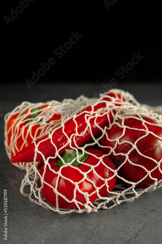 Red and orange peppers in a string bag on a dark background. Vegetables in a string bag