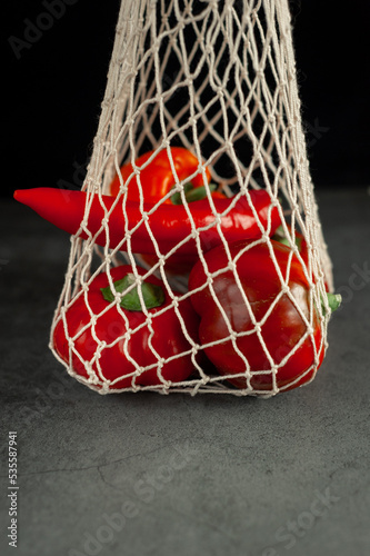 Red and orange peppers in a string bag on a dark background. Vegetables in a string bag