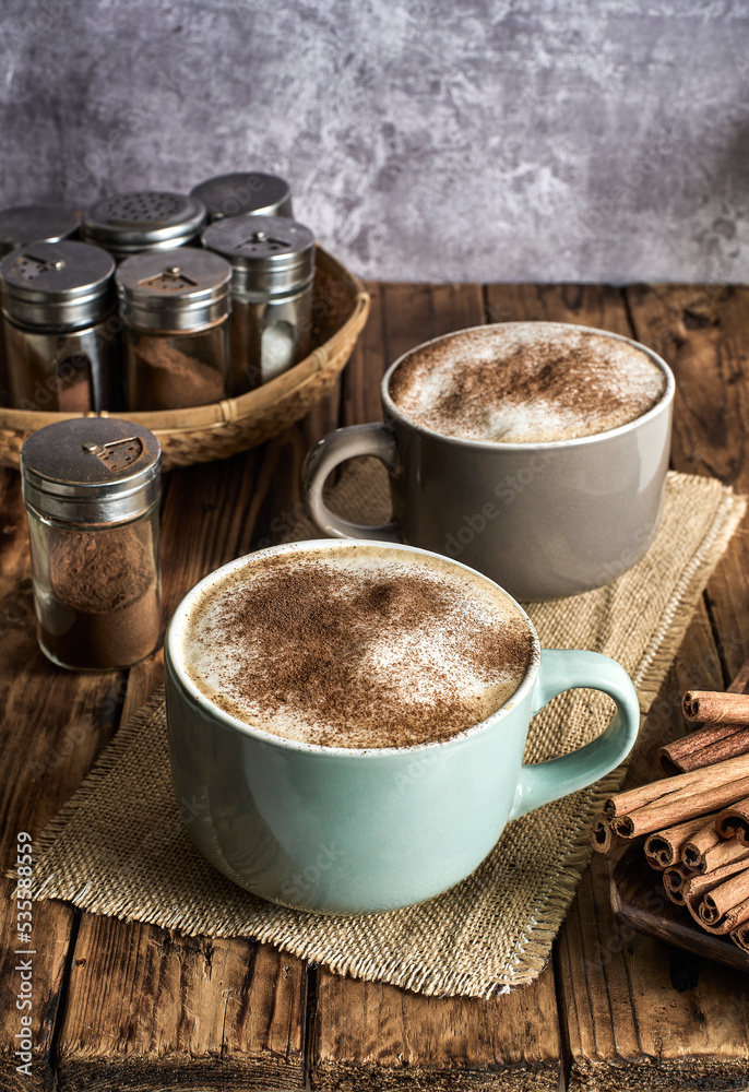 Two cups of Caffe Latte topped with cinnamon powder served in a cozy coffee shop. Two cups of Caffe Latte topped with cinnamon powder served in a cozy coffee shop.