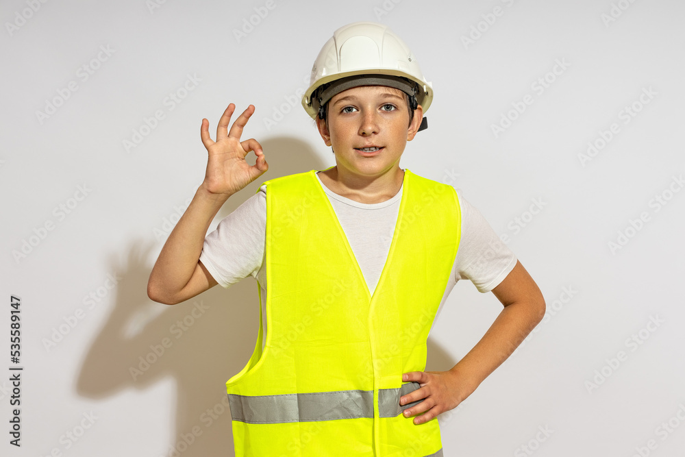 a teenager in a hardhat and a reflective vest shows an ok sign. a teenager in a hardhat and a reflective vest shows an ok sign.