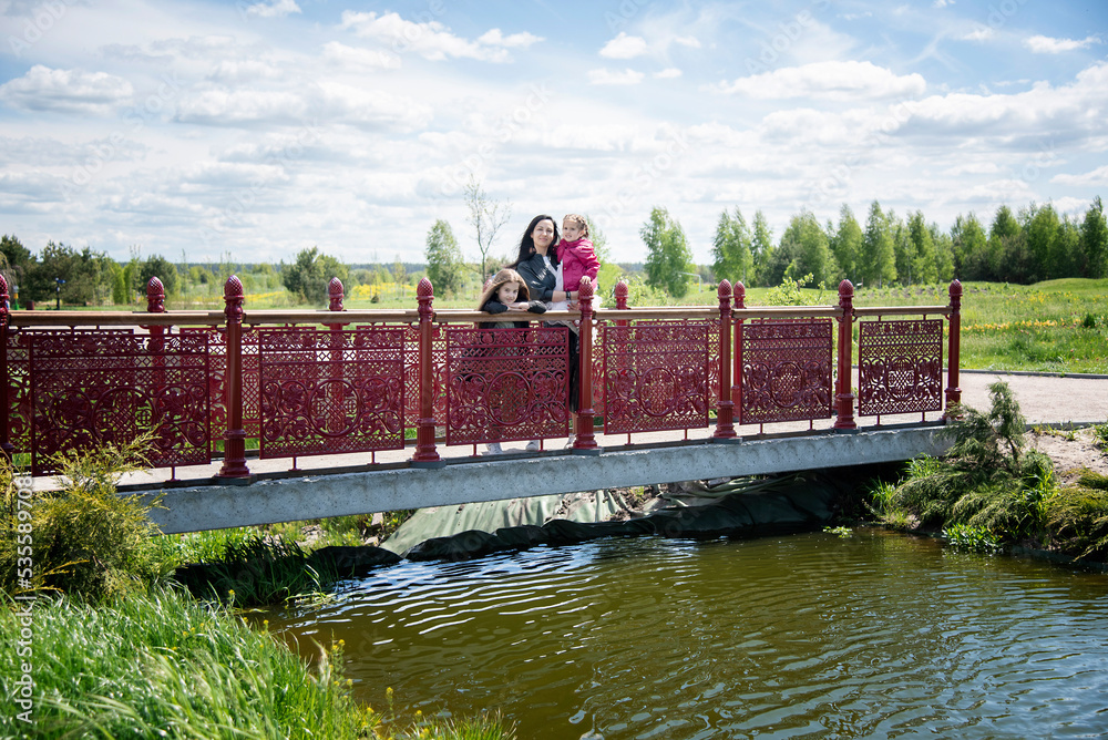 beautiful mother with children  on bridge over river on sunny day in summer park