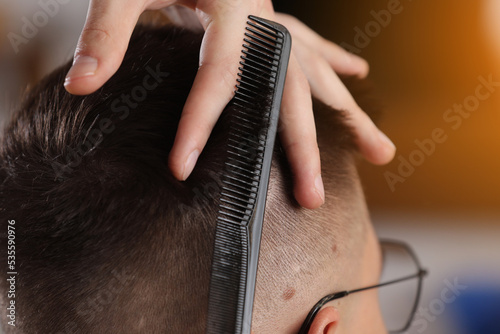 Hands of barber using scissors to cut customer's hair in salon. barber cuts hair, hairstyle. Male customer sitting in chair in hairdressing salon or barbershop. Creating new hair look.