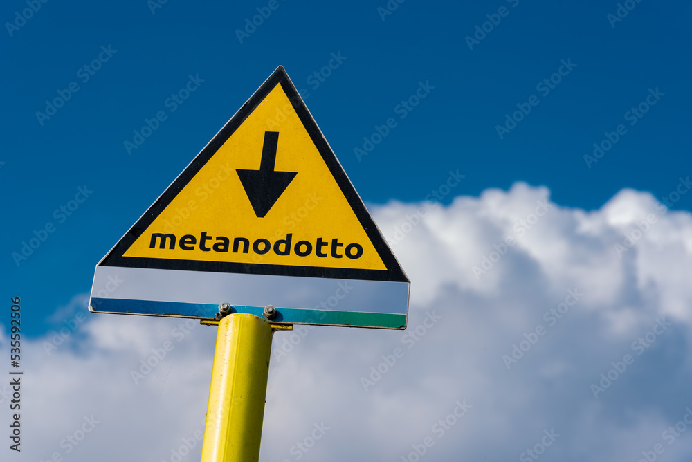 Sign indicating the presence of underground methane pipeline in Italy, metanodotto (gas pipeline) sign on blue sky and cloud Sign indicating the presence of underground methane pipeline in Italy, metanodotto (gas pipeline) sign on blue sky and cloud