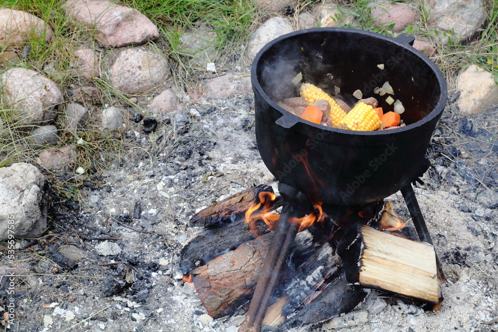 Pot full of meat and vegetables near campfire Pot full of meat and vegetables near campfire
