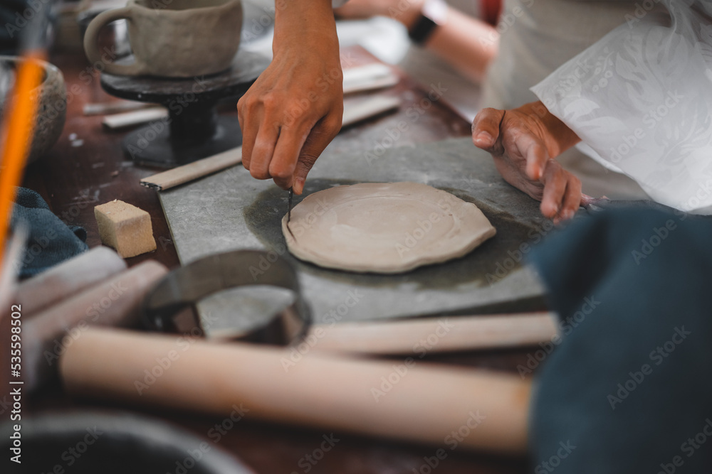 View of female hands works with clay makes future ceramic plate, ceramic artist makes classes of hand building in modern pottery workshop, creative people handcrafted design View of female hands works with clay makes future ceramic plate, ceramic artist makes classes of hand building in modern pottery workshop, creative people handcrafted design