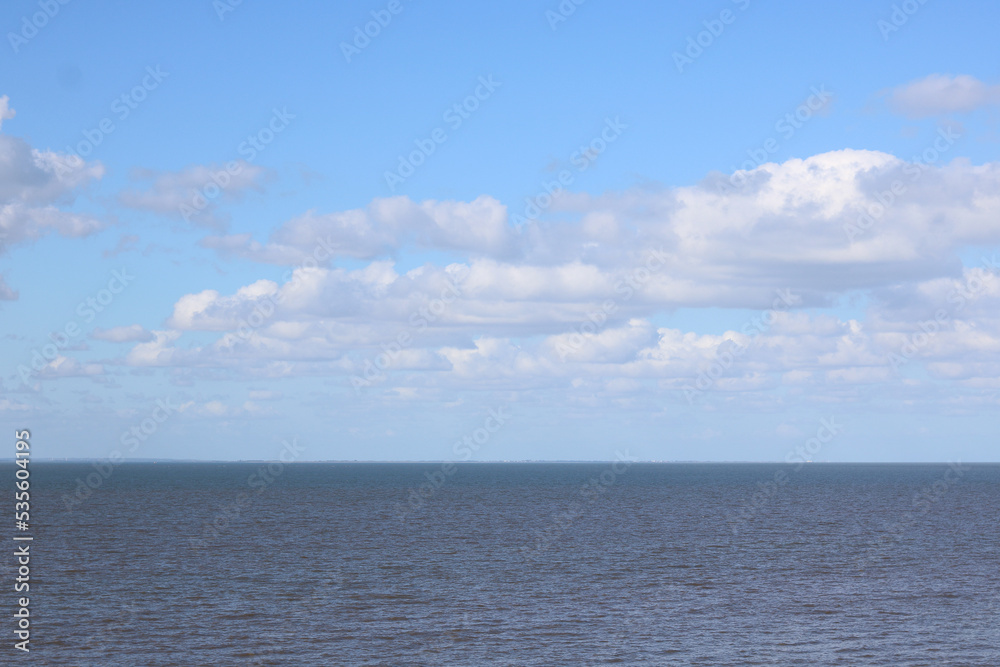 View out to sea with pale blue cloudy sky above dark water