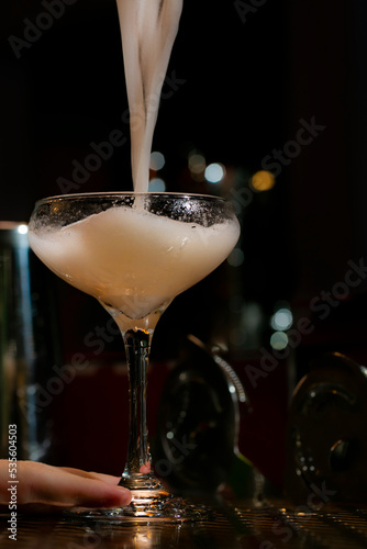 Fotografía Creamy egg white cocktail pouring into coupe glass on bar top
