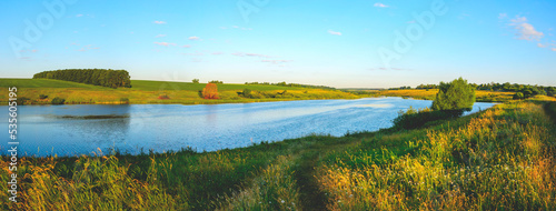 Summer sunny panoramic landscape with blue calm river and green farm fields