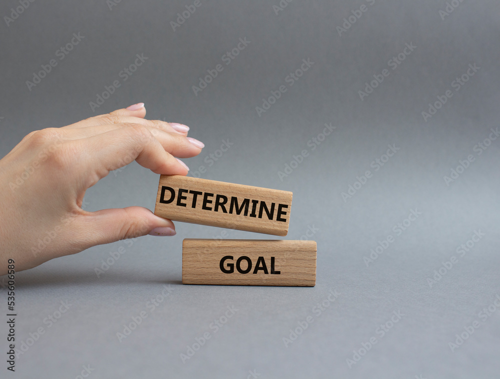 Determine goal symbol. Wooden blocks with words Determine goal. Beautiful grey background. Businessman hand. Business and Determine goal concept. Copy space. Determine goal symbol. Wooden blocks with words Determine goal. Beautiful grey background. Businessman hand. Business and Determine goal concept. Copy space.
