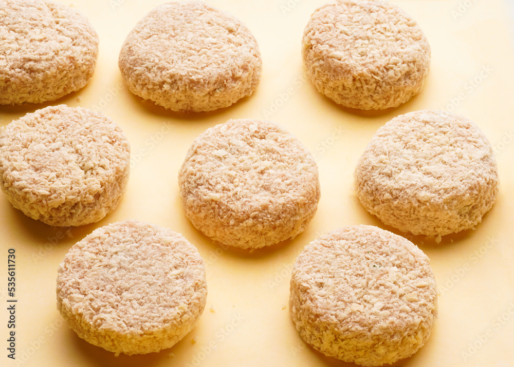 Raw blanks of round chicken cutlets in breading on a yellow background. Preparation for home dinner Raw blanks of round chicken cutlets in breading on a yellow background. Preparation for home dinner