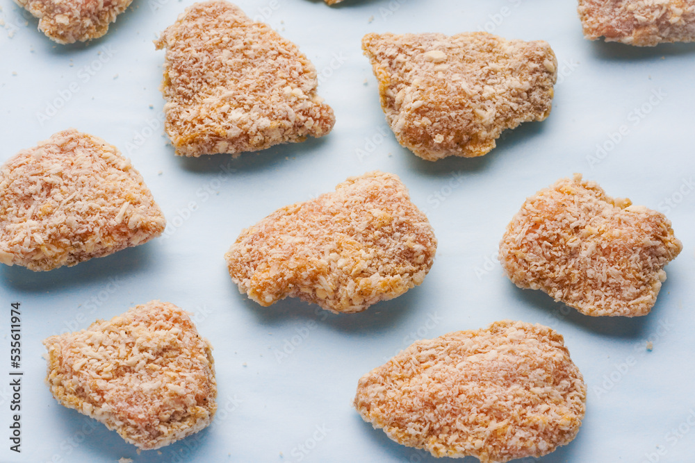 Raw frozen pieces of breaded chicken on a blue background. Semi-finished products for homemade nuggets
